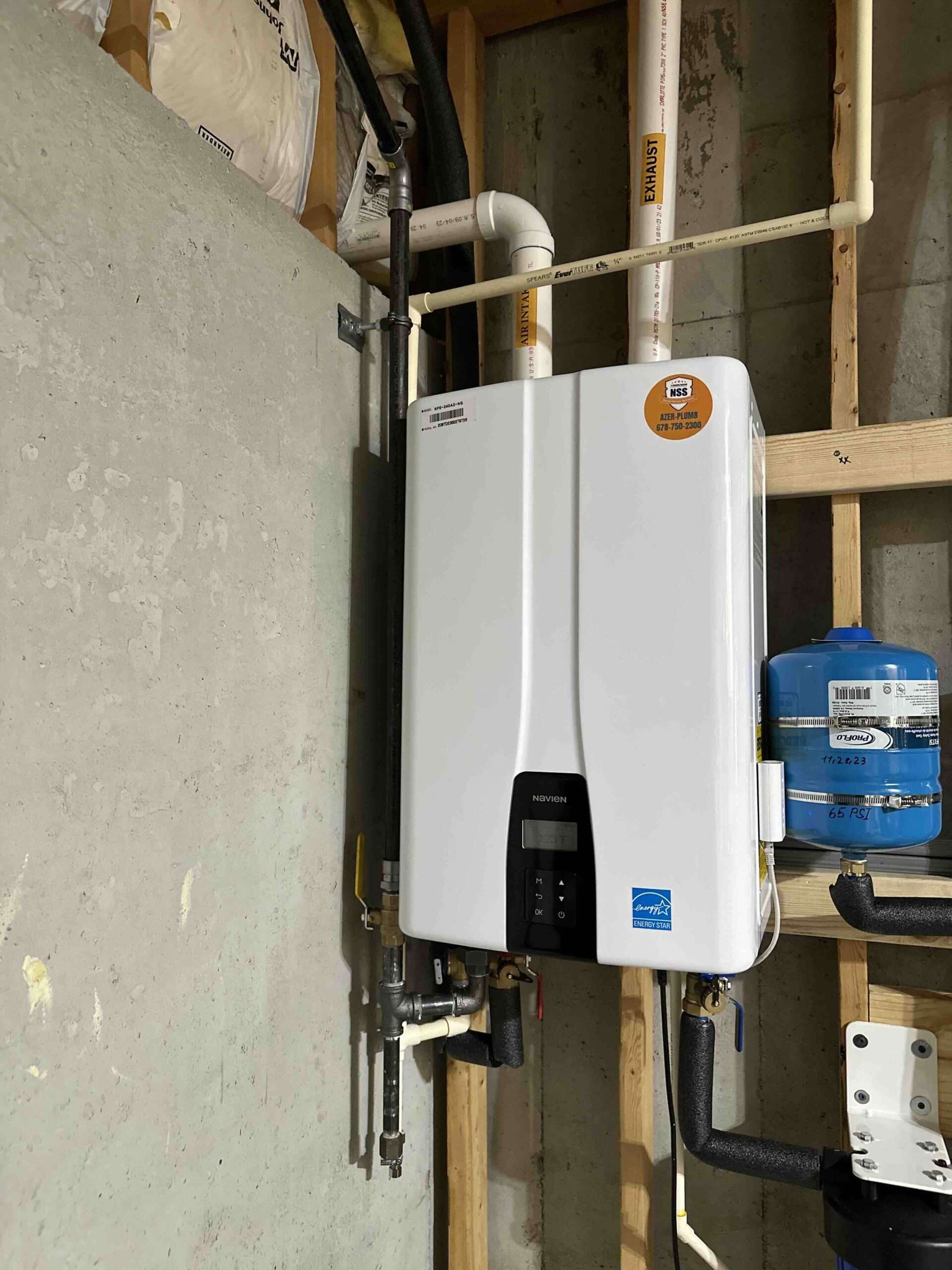 Tankless water heater mounted on a wall, featuring a sleek design and digital control panel, with plumbing connections visible, emphasizing energy efficiency and space-saving benefits.