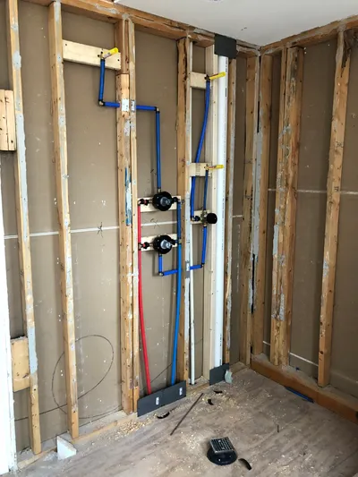 Water line installation with blue and red pipes mounted on wooden studs in a partially constructed wall, illustrating plumbing work relevant to leak detection and repair services.