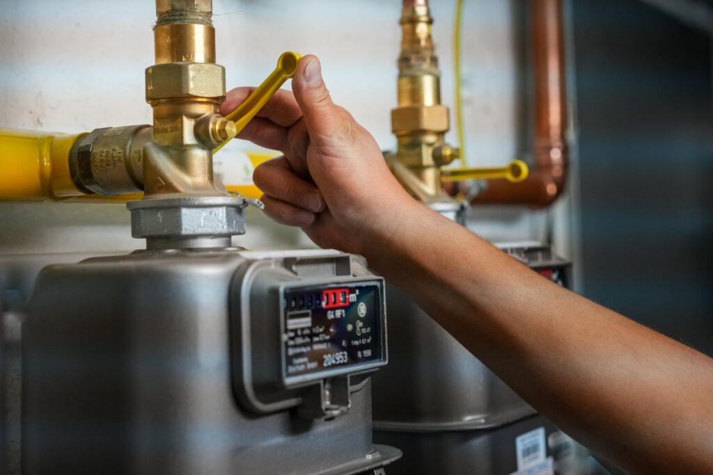 Hand adjusting a yellow gas valve connected to a gas meter, emphasizing gas line maintenance and safety in plumbing systems.