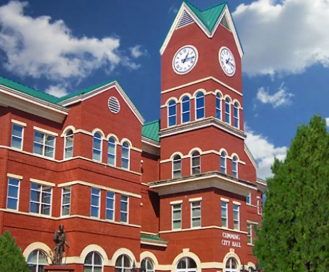 Cumming City Hall building with clock tower, red brick architecture, and green roof, representing Cumming, GA, a service area for Azerplumb plumbing services.