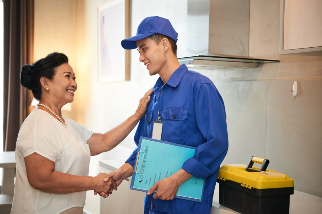 Licensed plumbing contractor shaking hands with a homeowner, discussing water line installation, with tools and service documents visible in a modern kitchen setting.