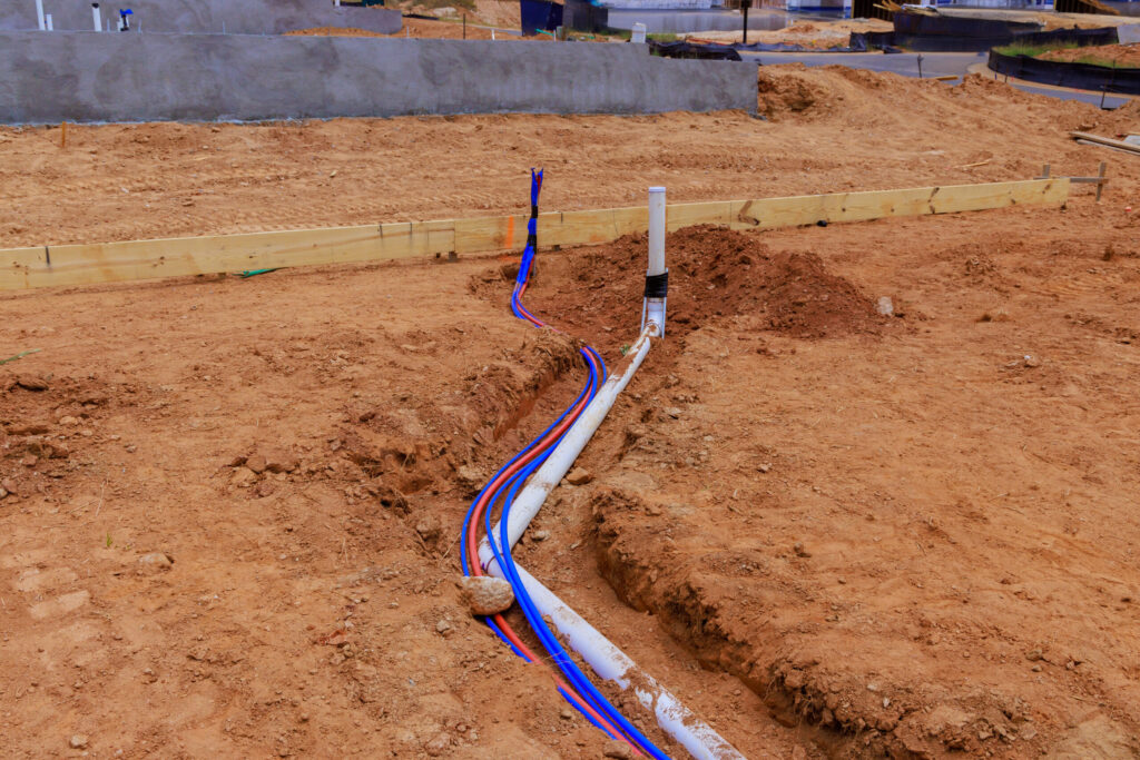 Underground water line installation with PVC and PEX pipes at a new construction site, ready for foundation pouring.