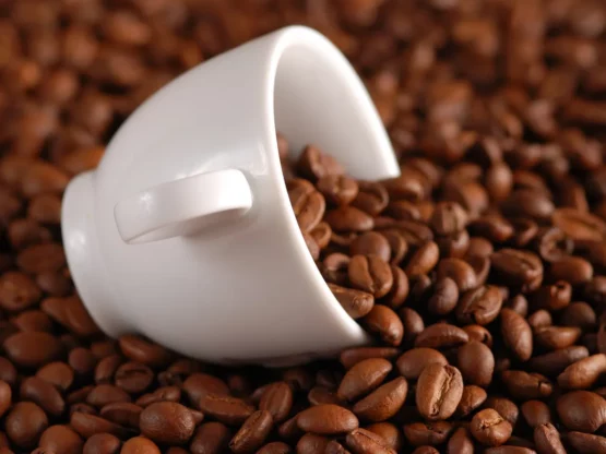 White coffee cup tipped over on a bed of coffee beans, illustrating the topic of coffee grounds disposal and potential plumbing issues.