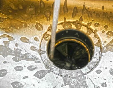 Water flowing into a kitchen sink with a visible garbage disposal unit, surrounded by bubbles and splashes, illustrating the importance of proper garbage disposal function for kitchen cleanliness.