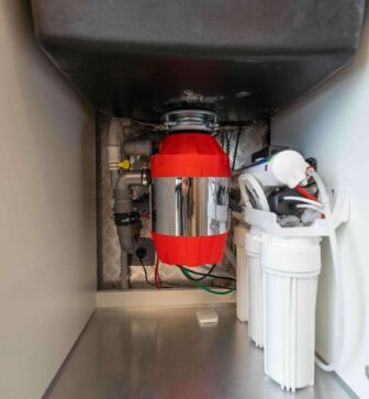 Garbage disposal unit installed under kitchen sink, featuring a red and silver design, with plumbing connections and water filtration system visible, relevant to Azerplumb's garbage disposal installation and repair services.