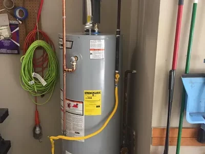 Water heater unit in a garage setting, featuring visible pipes and safety labels, relevant to energy-saving tips for homeowners considering vacation settings.