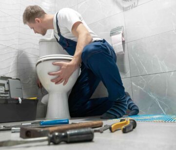 Plumber installing a toilet in a bathroom, surrounded by tools, demonstrating professional toilet installation services by Azerplumb.