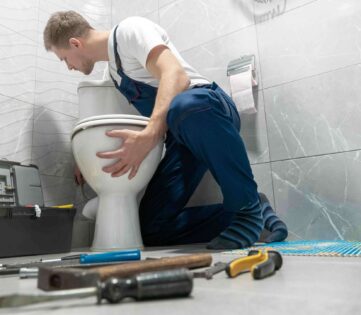 Plumber installing toilet in bathroom with tools nearby, emphasizing professional toilet installation and repair services in Dunwoody, GA.
