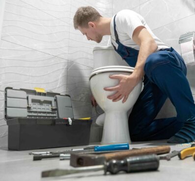 Plumber repairing a toilet with tools and a toolbox in a bathroom setting, emphasizing toilet repair services and maintenance solutions.