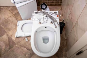 Toilet components and plumbing fixtures disassembled on a tiled bathroom floor, illustrating toilet repair services offered by Azerplumb in Roswell, GA.