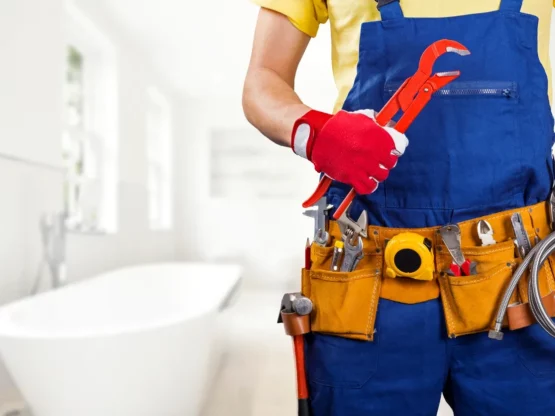 Professional plumber holding adjustable wrench and tools, ready to address plumbing issues in a bathroom setting.