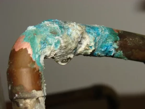 Corroded copper pipe with greenish copper oxide and limescale buildup, illustrating corrosion issues related to water composition.