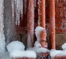 Frozen pipes with ice buildup and icicles, illustrating winter plumbing issues and risks of leaks and water damage.