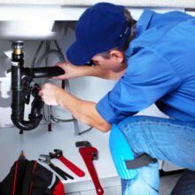 Plumber repairing pipes under a sink, showcasing tools like wrenches and a toolbox, representing Azerplumb's plumbing services in Cumming, GA.