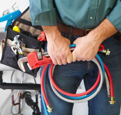 Plumber holding adjustable wrench and plumbing hoses, ready for tankless water heater installation and repair services in Atlanta, GA.