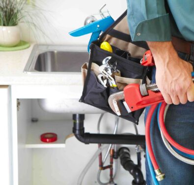 Plumber holding a tool belt filled with plumbing tools, standing near a kitchen sink, emphasizing expertise in tank water heater installation and repair services in Marietta, GA.