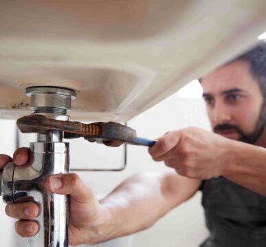 Plumber using a wrench to tighten a pipe under a sink, demonstrating professional plumbing services and expertise.
