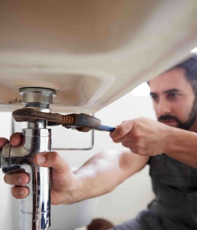 Man using a wrench to repair a sink's plumbing, illustrating professional plumbing services related to toilet installation and repair.