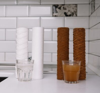 Water filter cartridges and glasses of filtered and unfiltered water on a kitchen countertop, illustrating the importance of reverse osmosis systems for clean drinking water.