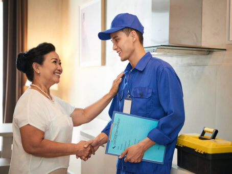 Plumber in blue uniform shaking hands with homeowner, discussing plumbing services and inspections in a residential setting.