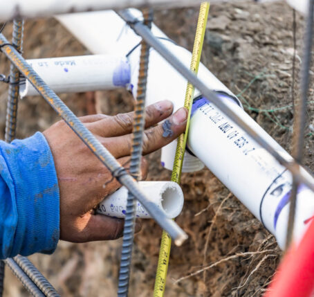 Hand measuring PVC pipes during water line installation, showcasing precise plumbing work and preparation for underground utility connections.